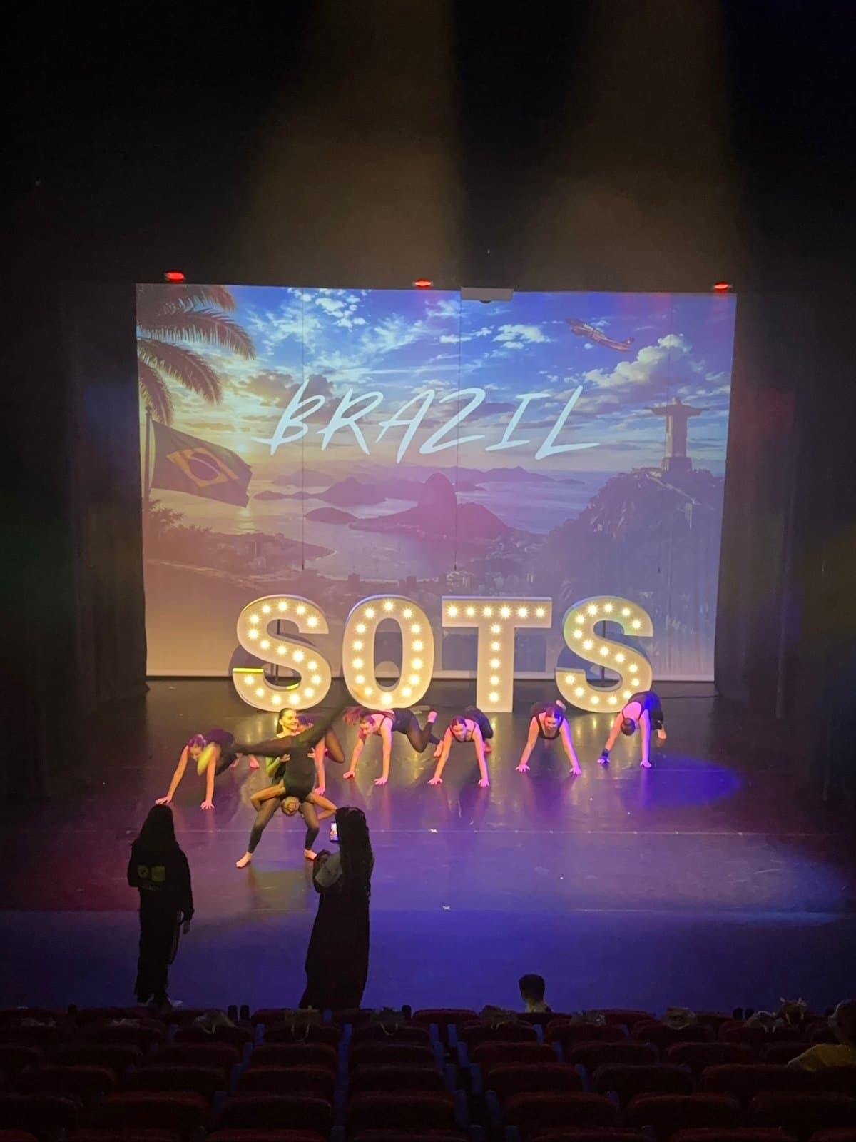 Senior acro dancers in a floor sequence on stage in front of a Brazil backdrop and SOTS letters